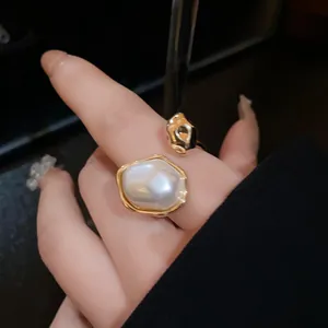 Close-up of elegant gold-plated open ring with large oval pearl on index finger.