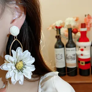 Close-up of a white fabric flower earring with raffia stud on model ear.