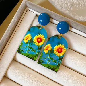 Detailansicht der blauen Acryl-Ohrringe mit leuchtenden Sonnenblumen-Aufdrucken.