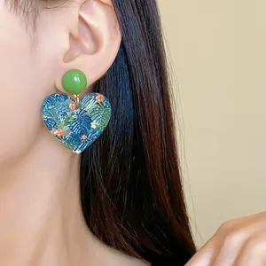 Nahaufnahme von herzförmigen Acrylohrringen mit lebendigen tropischen Blatt- und Blumenprints.