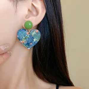 Detailaufnahme eines herzförmigen Ohrrings mit tropischem Blumendruck am Ohr des Models