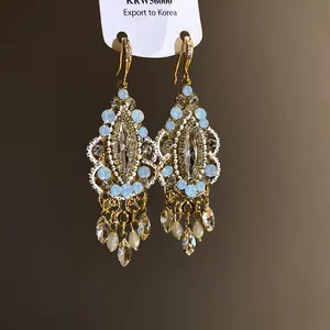 Close-up of ethnic style rhinestone drop tassel earrings with gold finish and light blue crystals