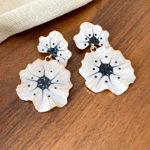 Elegant white enamel ginkgo leaf dangle earrings for women on a rustic wooden background texture