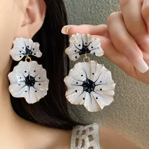 Detailed close-up view of white enamel ginkgo flower drop earrings with gold trim on model.