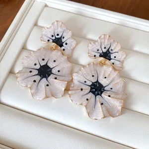 Detail view of elegant cream enamel ginkgo leaf dangle earrings with a refined gold trim.