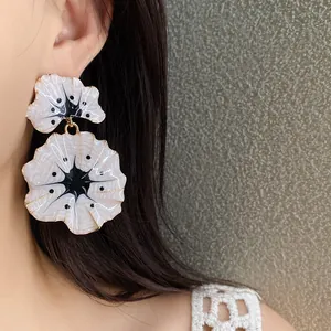 Detailed view of elegant cream white enamel ginkgo flower drop earrings worn by model