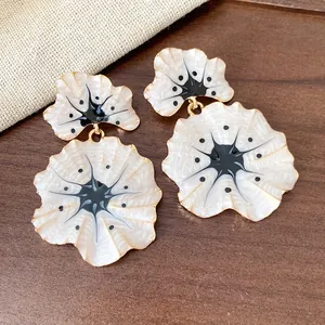 Close-up of elegant ginkgo flower drop earrings with white enamel and golden edges.
