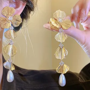Detailed macro view of gold flower petal earrings with zircons and teardrop pearls.