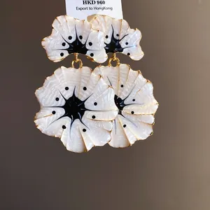 Close-up of elegant white ginkgo flower drop earrings with black enamel details.