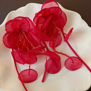 Dettaglio di orecchini a fiore in rete rossa con nappe di perline e nastri.