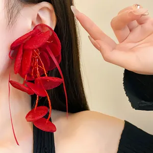 Dettaglio di un grande orecchino a fiore in rete rossa con nappe di perline su orecchio.