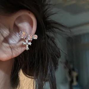 Close-up of zircon-studded ear cuff with a dangling cross pendant on model's ear.
