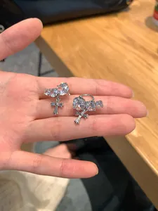 Detailed close-up of zircon-set silver ear cuffs with delicate cross pendants on a hand