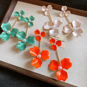 Nahaufnahme bunter Emaille-Blumenohrringe mit eleganten Perlenmitten im Holzrahmen