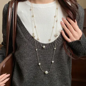 Elegant double-layered long pearl necklace worn over a grey knit sweater for winter