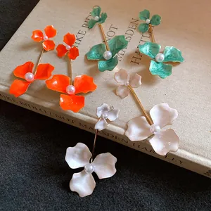 Detailansicht bunter Tropföl-Blumenohrringe mit Perlen auf einem Vintage-Buchhintergrund