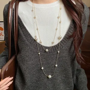 Detail view of a double-layer long necklace with asymmetrical pearls on a sweater