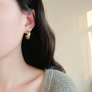 Minimalist gold metal hoop earrings with a twisted design shown on a female model