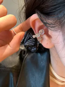 Close-up of silver-toned ear cuff with cubic zirconia and a cross pendant.