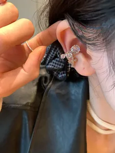 Close-up of a silver-toned ear cuff featuring round zirconia and a cross pendant