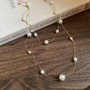 Detailed view of asymmetric pearl double-layer necklace draped over a vintage book.