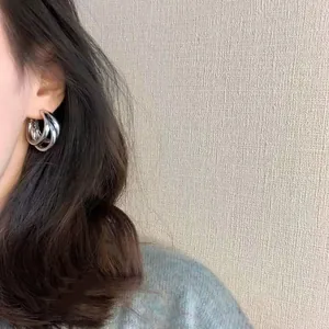 Side view detail shot of a woman wearing minimalist silver interwoven hoop earrings