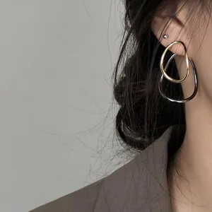 Close-up detail of minimalist asymmetric metallic teardrop hoop earrings in gold and gunmetal