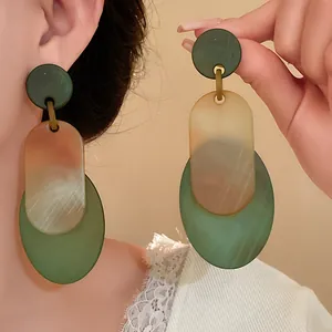 Close-up of vintage green and amber oval acrylic dangle earrings with marble texture