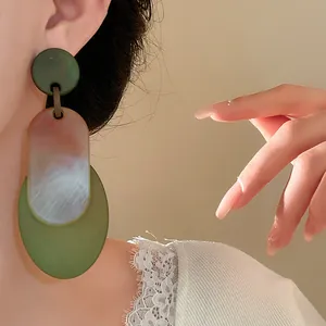 Close-up of geometric acrylic drop earrings with green and marble patterns