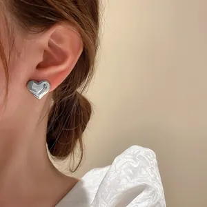 Detail of minimalist silver-finish heart-shaped stud earring worn on model's ear