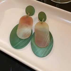 Close-up of vintage oval acrylic earrings featuring green and marble marble textures on a tray