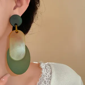 Close-up of vintage oval acrylic drop earrings in green and amber on an Asian model