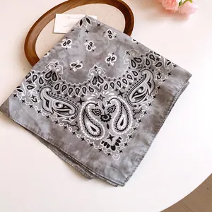 Close-up of a gray bandana with intricate paisley and floral patterns on a wooden tray