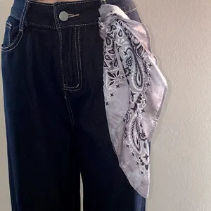 Macro detail view of a grey paisley print bandana tied to dark denim jeans belt loop