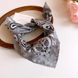 Close-up of a gray paisley print bandana scarf on a decorative wooden tray.