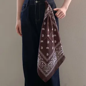 Elegant brown paisley print silk scarf styled as a chic fashion accessory on dark denim jeans