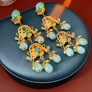 Close-up of vintage court-style earrings with green stones and gold floral details.