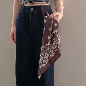 Detail shot of a brown paisley bandana with sunflower print tied to denim jeans.