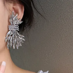 Close-up of large sparkling crystal wing earrings worn on model's ear for luxury party look.