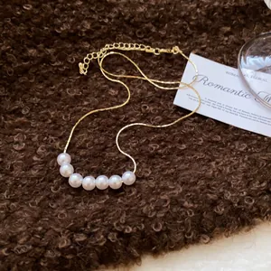 Close-up of French vintage gold necklace with seven elegant white pearls on brown texture.