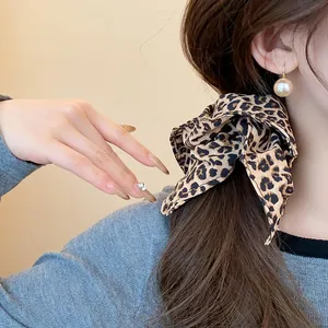 Dettaglio di un elastico per capelli leopardato con estremità a fiocco sui capelli.