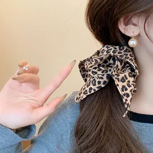 Dettaglio di un elastico per capelli leopardato vintage con fiocco su capelli castani.