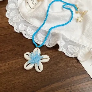 Detailansicht einer handgefertigten blauen Perlenkette mit weißem Muschel-Anhänger
