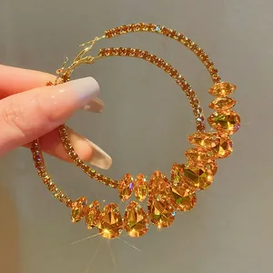 Close-up of oversized gold-tone hoop earrings with sparkling amber water-drop crystals.