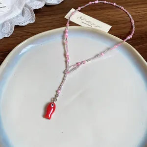 Nahaufnahme einer rosa Perlenkette mit einem roten Fisch-Anhänger auf einem Teller