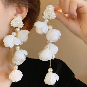 Close-up of elegant long dangle earrings with white fabric flowers and pearls.