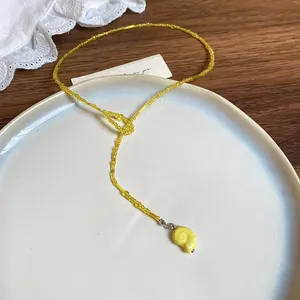 Nahaufnahme einer gelben Perlenkette mit einem zierlichen Anhänger in Form einer Muschel.