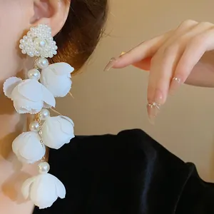 Close-up detail of elegant white fabric flower and pearl drop earrings on a model's ear.