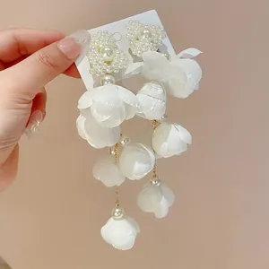Macro view of white fabric flower petals and pearl heart design on elegant dangle earrings