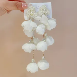 Close-up detail showing the elegant white fabric flower and faux pearl long drop earrings
